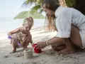 Bambina bionda e mamma giocano con secchiello e paletta sulla sabbia. Un'idea su cosa portare al mare con bambini per divertirsi.