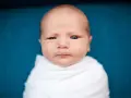 Primo piano di un neonato avvolto in una coperta bianca. La sua testa è quasi calva, mostrando una leggera perdita capelli neonato, tipica dei primi mesi.