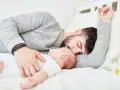 Padre e neonato nel lettone in sicurezza, un momento di dolce riposo e amore.