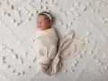 Dolce bambino in fasce dorme sereno su una coperta bianca decorata con pompon e nappine.