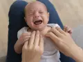 Un neonato piange disperato, le mani di un adulto cercano di calmarlo. Nessun danno tv neonati visibile, solo un momento di fragilità.