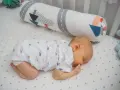 Dolce neonato dorme a pancia in giù, avvolto in un pigiamino con balene. Un cuscino decorato con navi lo accompagna nel sonno.