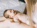 Un bimbo sorride sdraiato sulle gambe della mamma. Forse è l'inizio della lallazione, con le prime vocali che risuonano nell'aria.