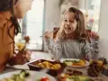 Bambina felice mangia da sola a tavola, mostrando che a che età i bambini mangiano da soli è un traguardo raggiunto con gioia.