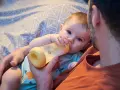 Un padre tiene un biberón per dare da mangiare al suo neonato. Il bambino afferra il biberon con le sue manine.