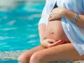 Pancia di donna incinta che si rinfresca in piscina, alleviando il caldo in gravidanza.