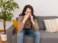 Donna seduta sul divano, con le mani sul naso, soffre di vestibolite nasale.