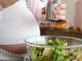 Donna incinta condisce un'insalata fresca. Ricorda come lavare frutta e verdura in gravidanza per una dieta sana.