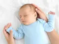 Un adorabile neonato dorme sereno sul fianco, cullato da mani amorevoli su una coperta bianca.