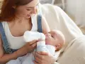 Mamma con capelli rossi allatta il suo bambino con un biberon. Impara come lavare i biberon per garantire l'igiene.