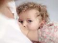 Bambina con occhi azzurri e capelli ricci, stretta al petto della madre. Un'immagine che evoca il legame profondo, ma anche le possibili conseguenze psicologiche dell'allattamento prolungato.