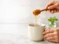 Miele che cola da un bastoncino in una tazza fumante, un rimedio naturale per la tosse.