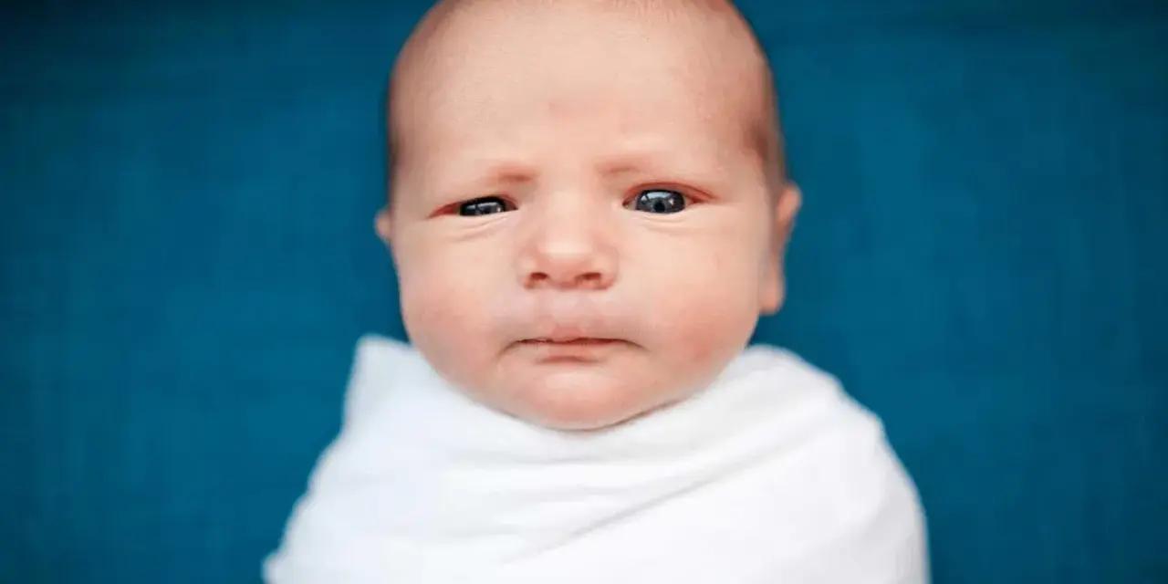 Primo piano di un neonato avvolto in una coperta bianca. La sua testa è quasi calva, mostrando una leggera perdita capelli neonato, tipica dei primi mesi.
