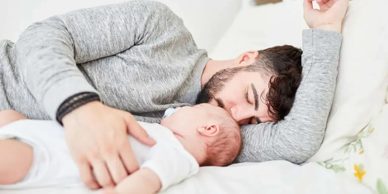 Padre e neonato nel lettone in sicurezza, un momento di dolce riposo e amore.