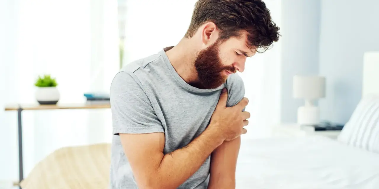 Uomo con barba che si tiene il braccio sinistro, avvertendo un fastidioso formicolio.