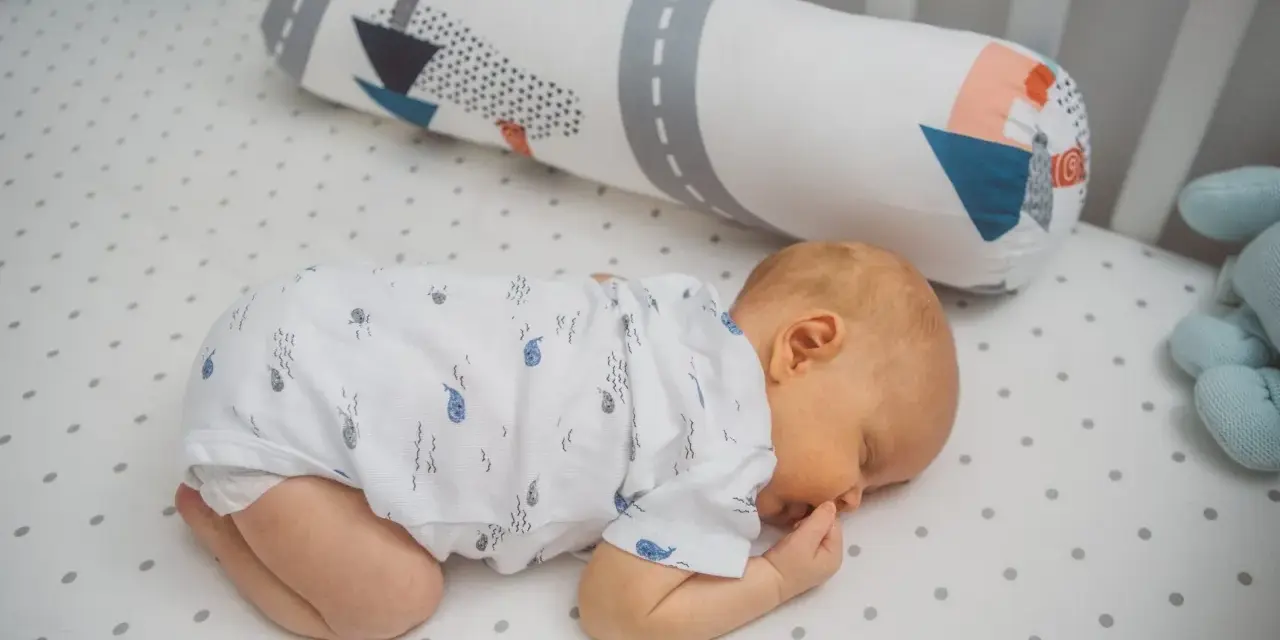 Dolce neonato dorme a pancia in giù, avvolto in un pigiamino con balene. Un cuscino decorato con navi lo accompagna nel sonno.