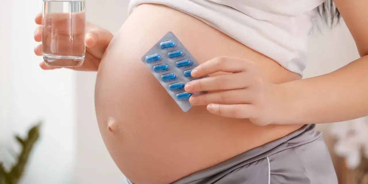 Pancia di donna incinta con blister di pillole blu e bicchiere d'acqua. Essenziale acido folico prima della gravidanza per la salute.