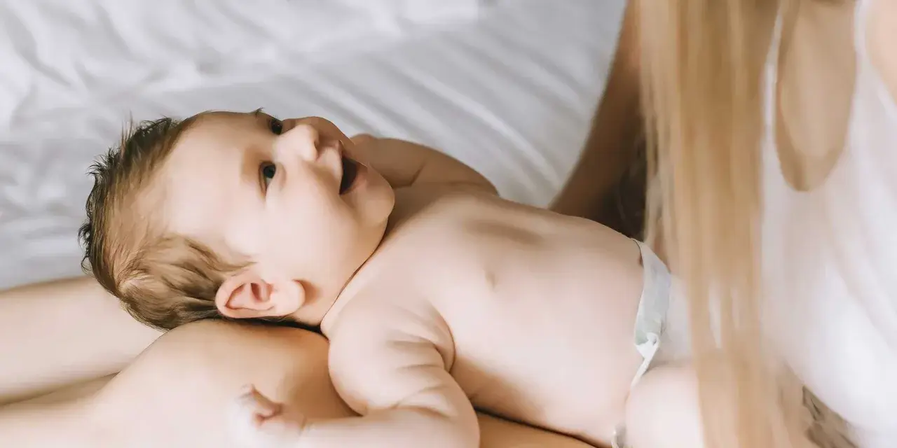 Un bimbo sorride sdraiato sulle gambe della mamma. Forse è l'inizio della lallazione, con le prime vocali che risuonano nell'aria.