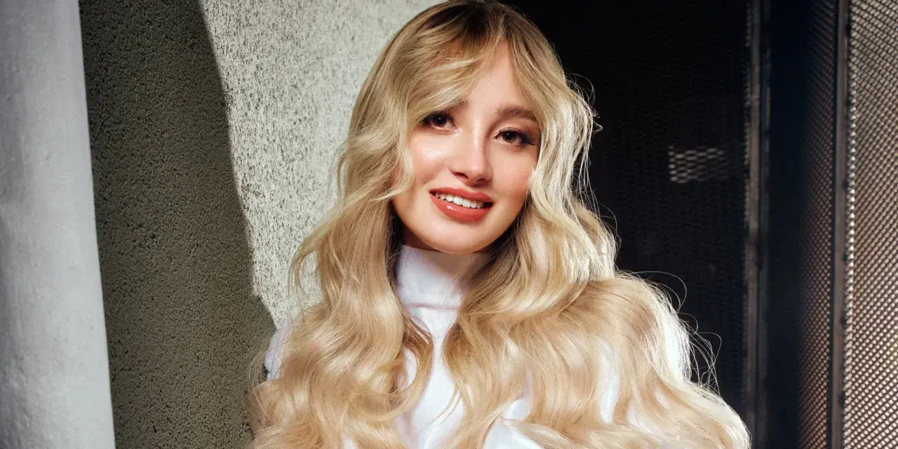Ragazza con lunghi capelli biondi mossi, un sorriso radioso e labbra luminose. Nuovi colori per capelli che esaltano la sua bellezza naturale.