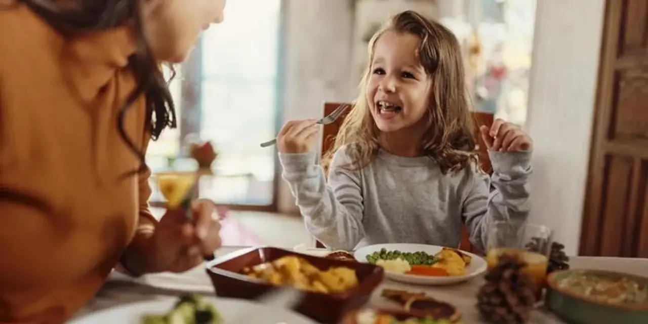 Bambina felice mangia da sola a tavola, mostrando che a che età i bambini mangiano da soli è un traguardo raggiunto con gioia.