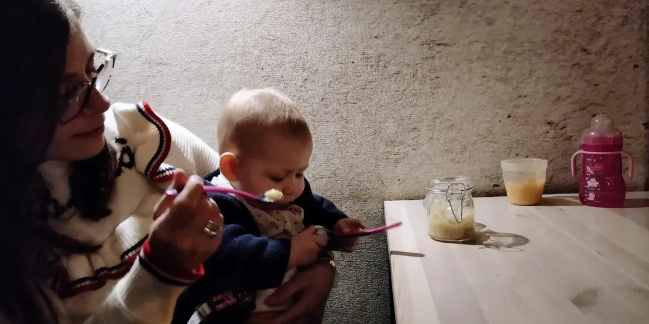 Mamma dà la pappa al suo bimbo fuori casa, con un vasetto di omogeneizzato e un biberon pronti.