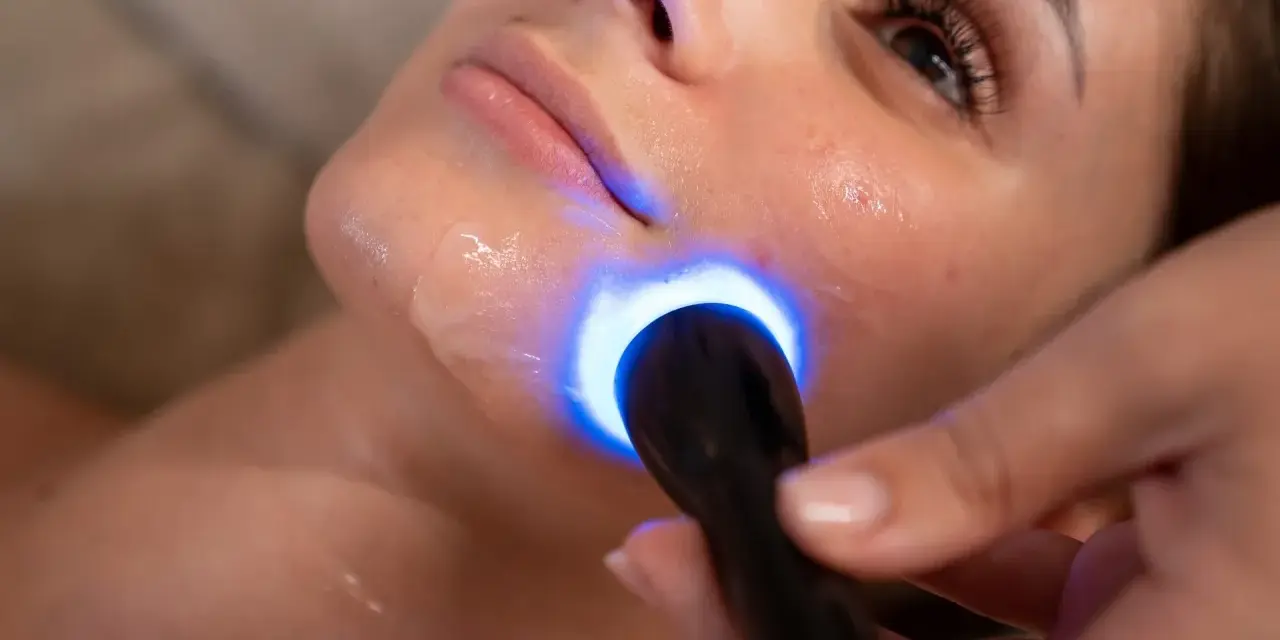 Primo piano del viso di una donna durante un trattamento di biorivitalizzazione con luce blu.
