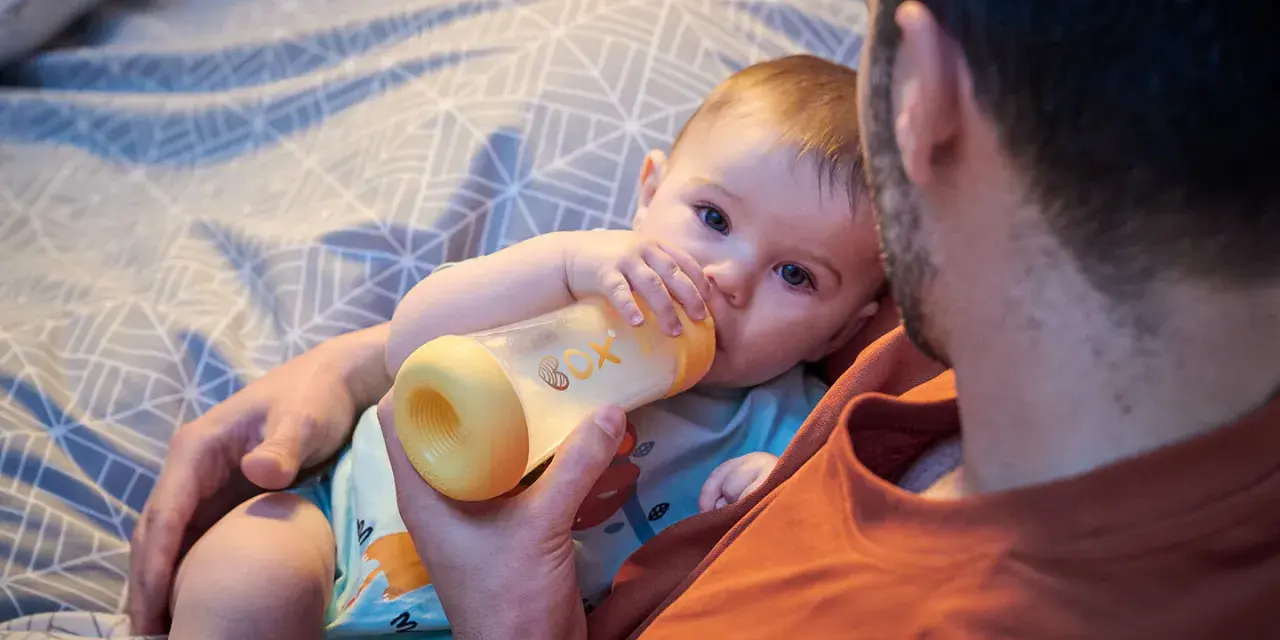Un padre tiene un biberón per dare da mangiare al suo neonato. Il bambino afferra il biberon con le sue manine.