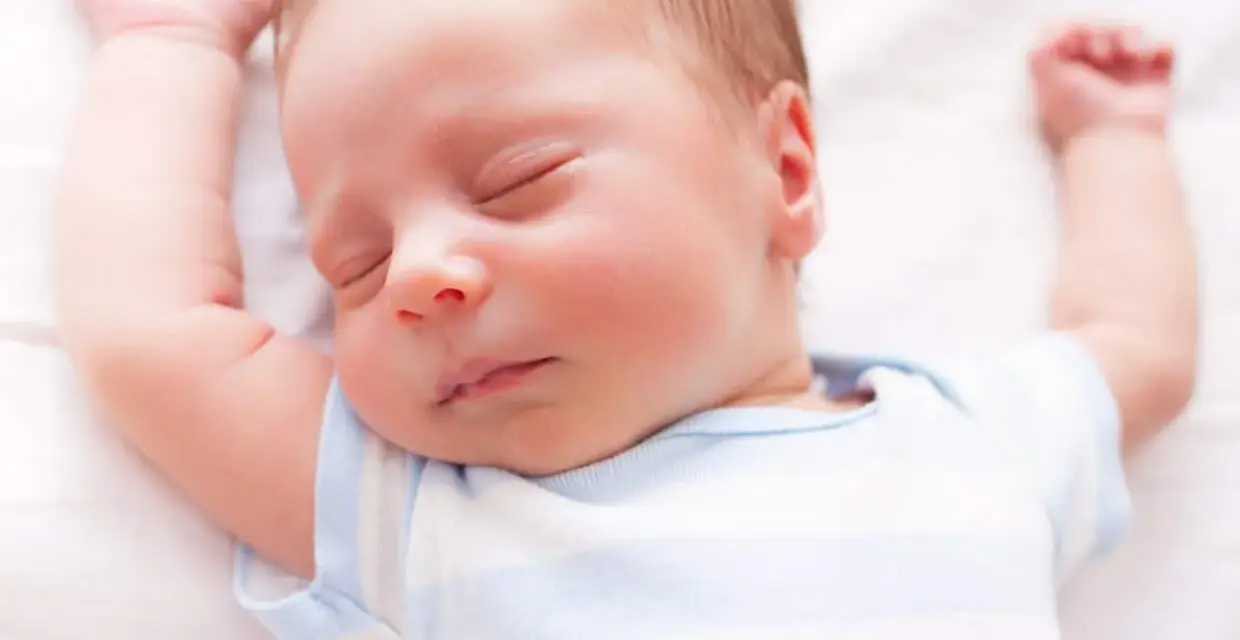 Un neonato dorme sereno con le braccia alzate. Sembra che i neonati possano mangiare mentre dormono, un vero miracolo della natura.