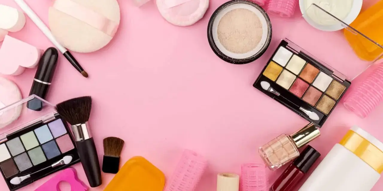 Tanti prodotti per il make-up, tra cui ombretti, rossetti e pennelli, disposti su sfondo rosa. Attenzione, gli ombretti scadono!