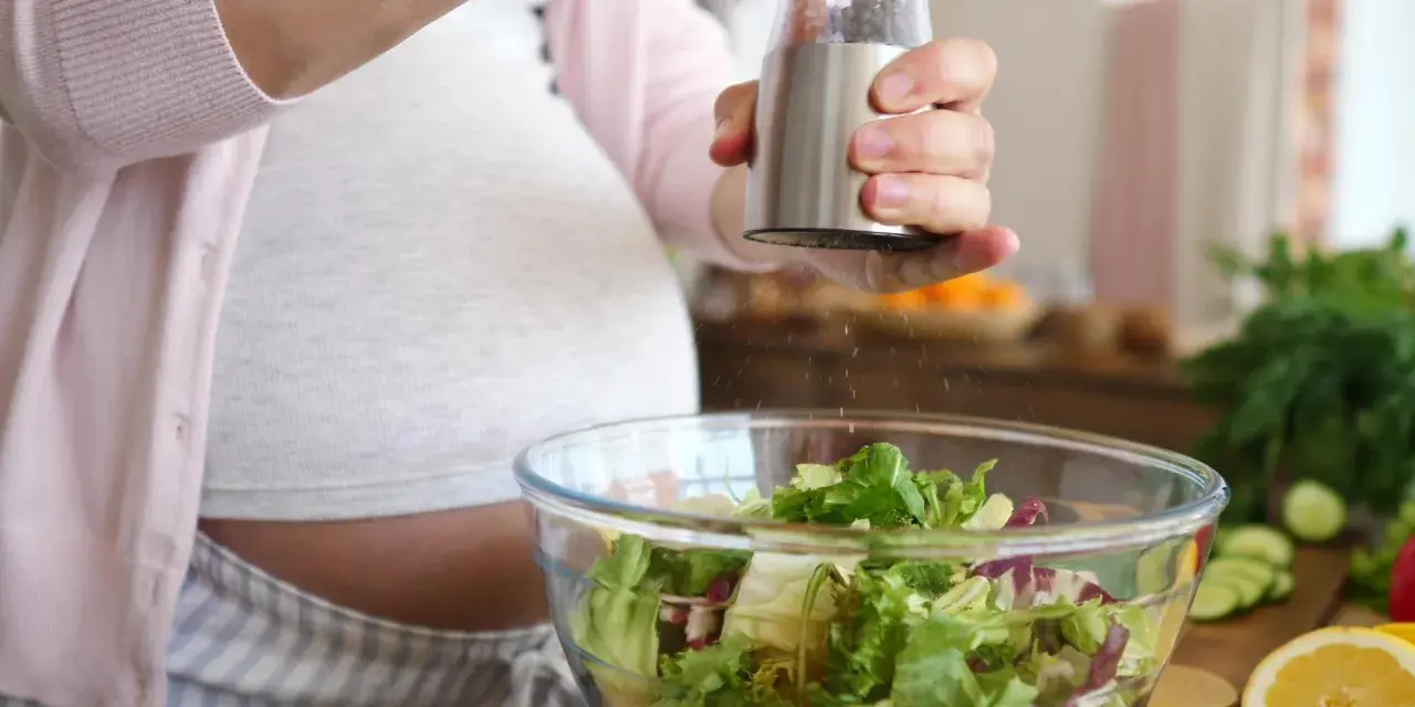 Donna incinta condisce un'insalata fresca. Ricorda come lavare frutta e verdura in gravidanza per una dieta sana.