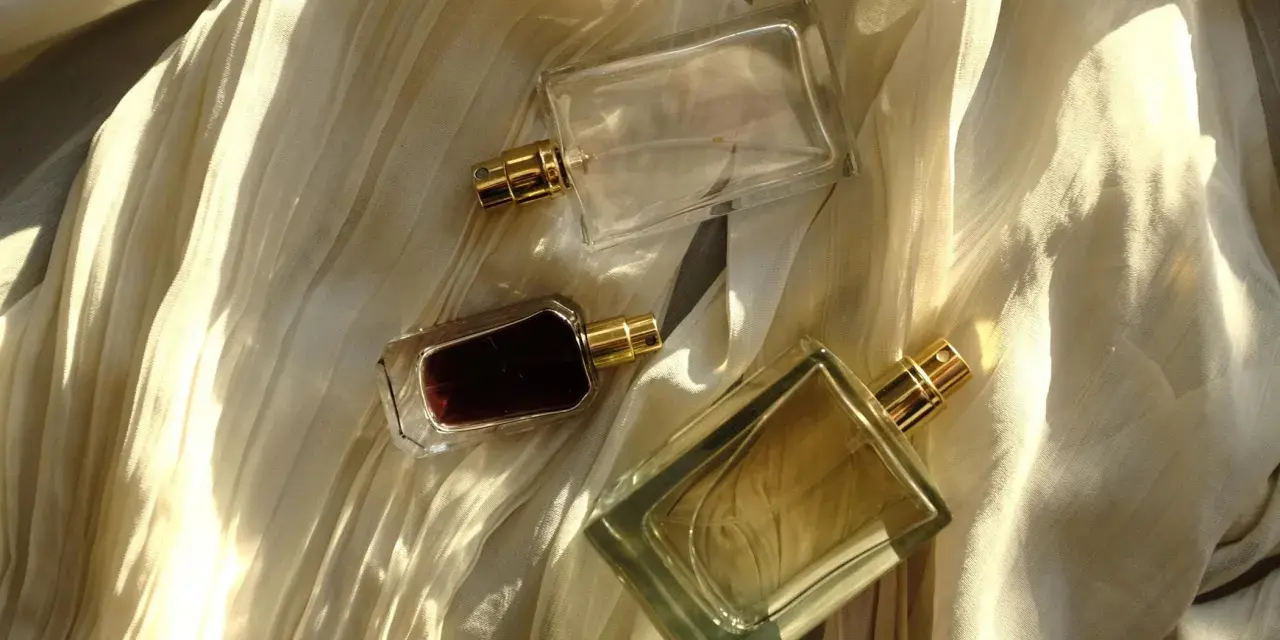 Flaconi di profumo su tessuto drappeggiato. Scopri come far durare di più il profumo con questi consigli.