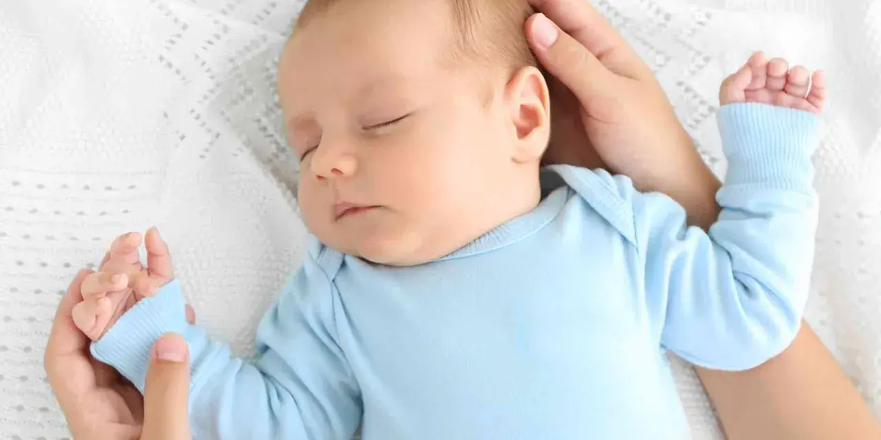Un adorabile neonato dorme sereno sul fianco, cullato da mani amorevoli su una coperta bianca.