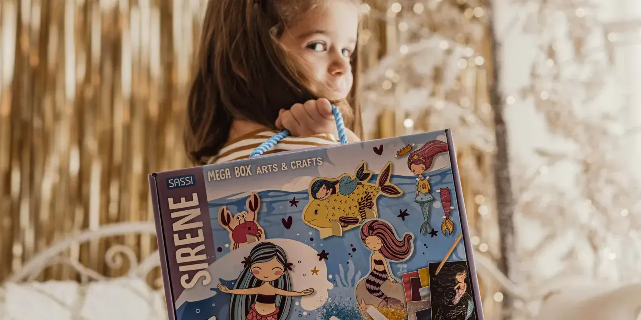 Bambina con scatola "Sirene Mega Box Arts & Crafts". A che età si impara a leggere? Forse con questo kit creativo, l'apprendimento sarà più divertente!