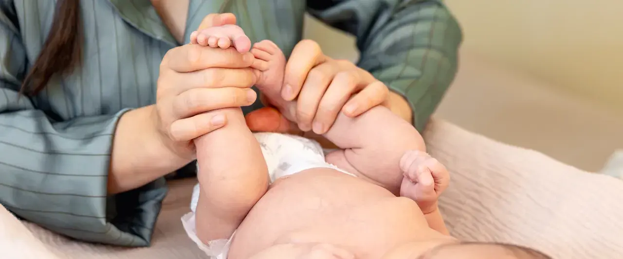Mani che massaggiano le gambine di un neonato, un gesto d'amore per capire se il neonato ha le coliche e alleviare il suo disagio.