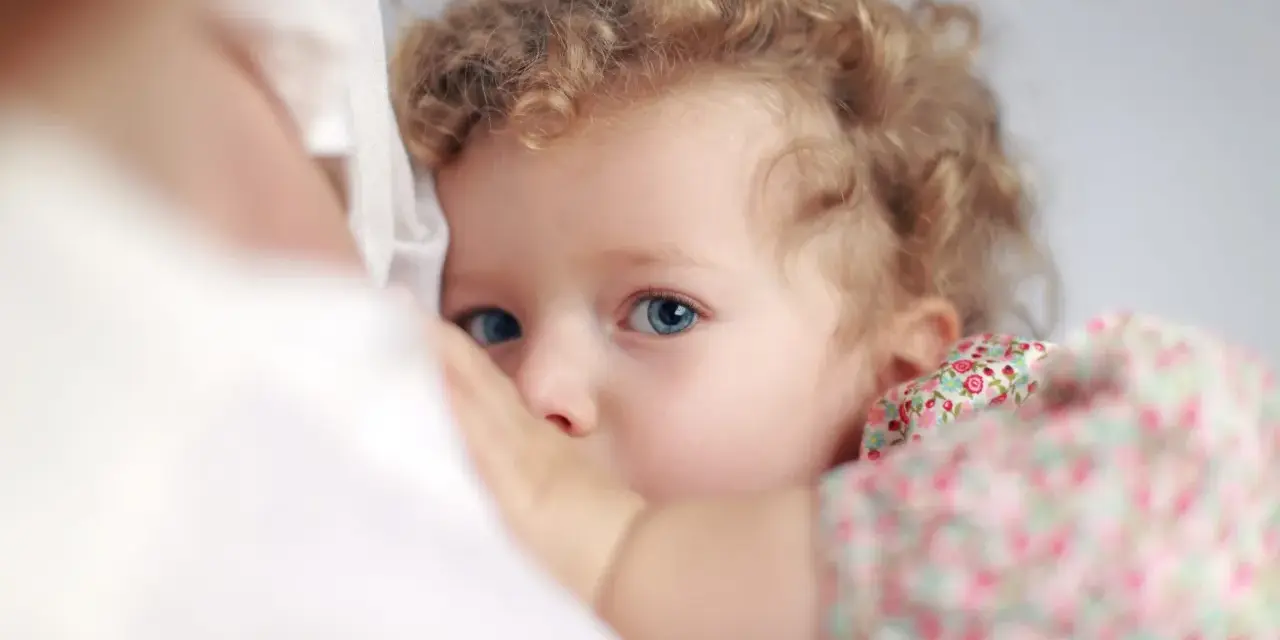 Bambina con occhi azzurri e capelli ricci, stretta al petto della madre. Un'immagine che evoca il legame profondo, ma anche le possibili conseguenze psicologiche dell'allattamento prolungato.