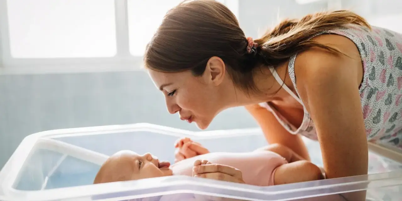 Mamma sorride al suo neonato nella culla. Un momento dolce che fa pensare a cosa mangiare dopo il parto per recuperare le energie.