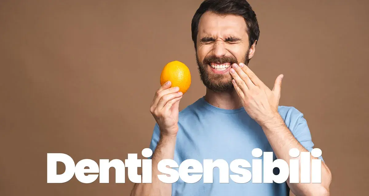 Uomo con espressione sofferente, tiene un'arancia e si tocca la guancia, mostrando i suoi denti sensibili al freddo.