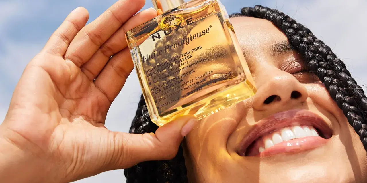 Una mano tiene una bottiglietta di Nuxe Huile Prodigieuse, un olio multiuso per viso, corpo e capelli. Scopri a cosa serve questo prezioso olio.