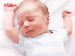 Un neonato dorme sereno con le braccia alzate. Sembra che i neonati possano mangiare mentre dormono, un vero miracolo della natura.
