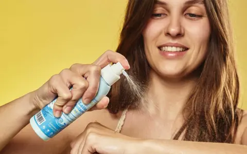 Donna sorridente applica latte solare spray SPF 50. La scelta di quale crema solare scegliere è facile con questo prodotto.