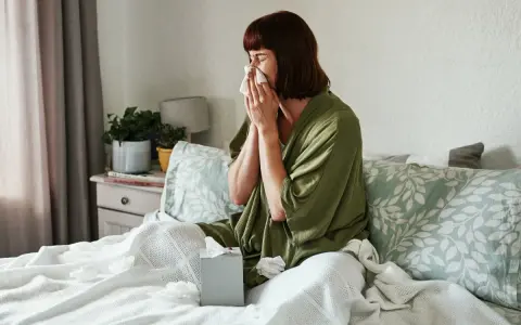 Donna a letto con fazzoletto, soffre di un raffreddore che non passa. Fazzoletti usati sparsi sul letto.