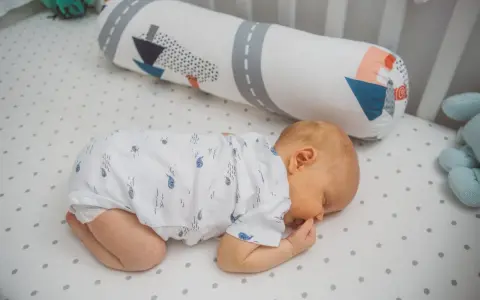 Dolce neonato dorme a pancia in giù, avvolto in un pigiamino con balene. Un cuscino decorato con navi lo accompagna nel sonno.