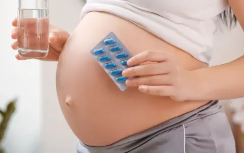 Pancia di donna incinta con blister di pillole blu e bicchiere d'acqua. Essenziale acido folico prima della gravidanza per la salute.