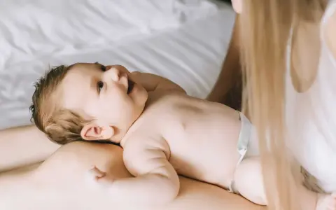 Un bimbo sorride sdraiato sulle gambe della mamma. Forse è l'inizio della lallazione, con le prime vocali che risuonano nell'aria.
