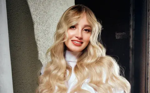 Ragazza con lunghi capelli biondi mossi, un sorriso radioso e labbra luminose. Nuovi colori per capelli che esaltano la sua bellezza naturale.