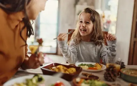 Bambina felice mangia da sola a tavola, mostrando che a che età i bambini mangiano da soli è un traguardo raggiunto con gioia.