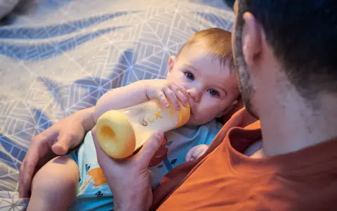 Un padre tiene un biberón per dare da mangiare al suo neonato. Il bambino afferra il biberon con le sue manine.
