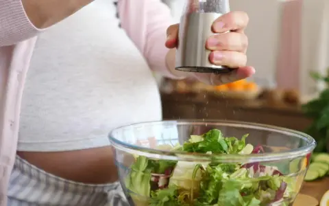 Donna incinta condisce un'insalata fresca. Ricorda come lavare frutta e verdura in gravidanza per una dieta sana.