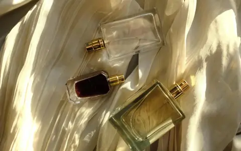 Flaconi di profumo su tessuto drappeggiato. Scopri come far durare di più il profumo con questi consigli.