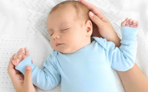 Un adorabile neonato dorme sereno sul fianco, cullato da mani amorevoli su una coperta bianca.